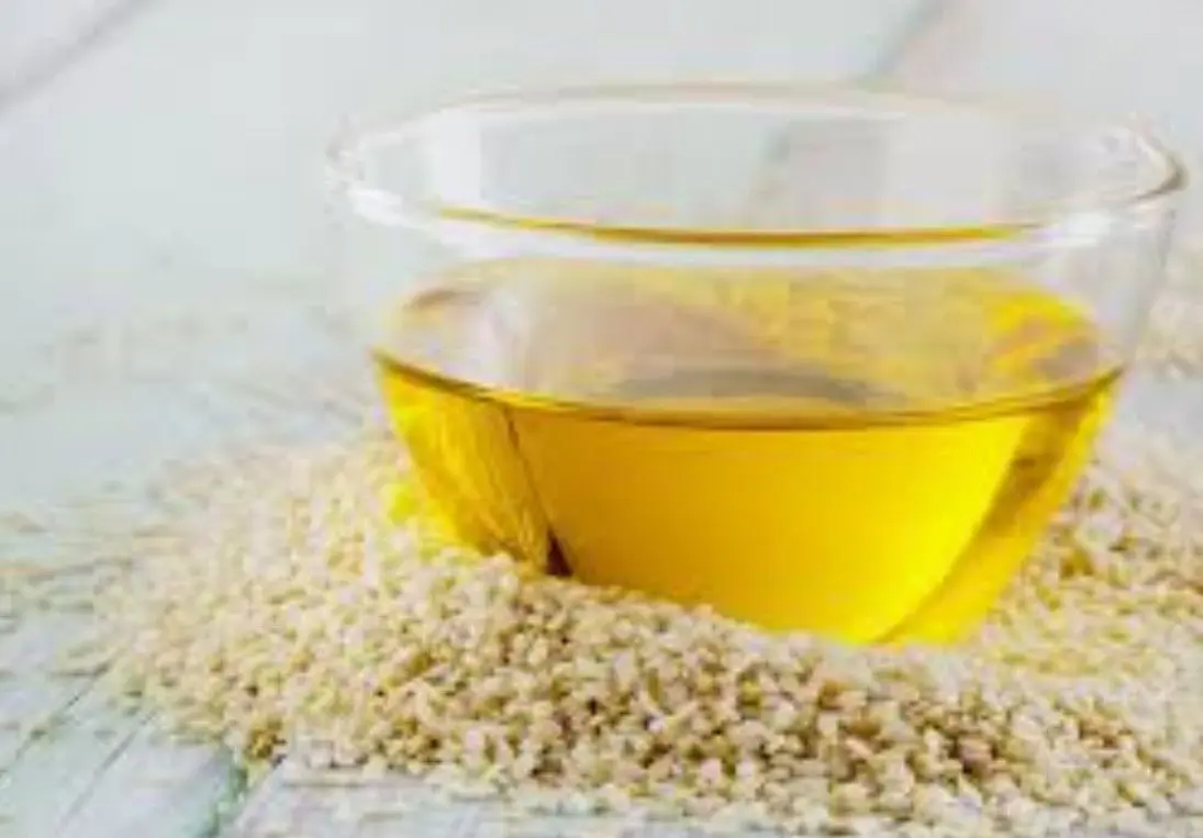 روغن کنجد در ظرف شیشه‌ای با دانه‌های کنجد اطراف آن