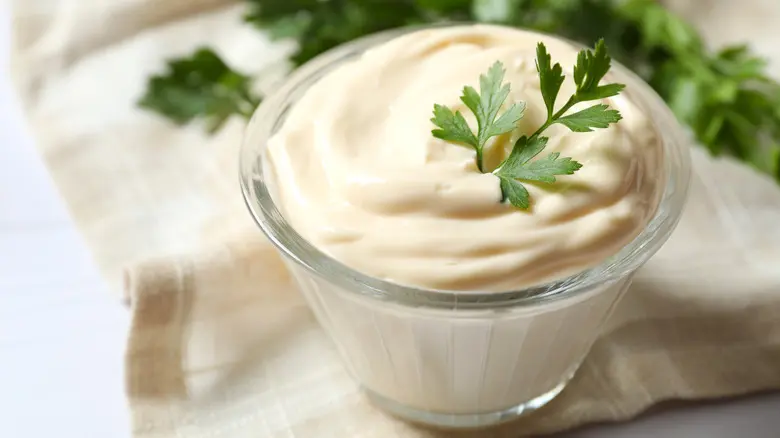مایونز در یک ظرف شیشه‌ای با لöffel چوبی و سالاد کالباس در کنار آن