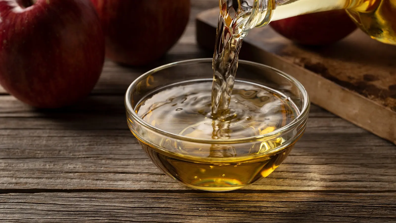 یک لیوان سرکه سیب با یک قاشق چایخوری و یک سیب تازه در کنار آن