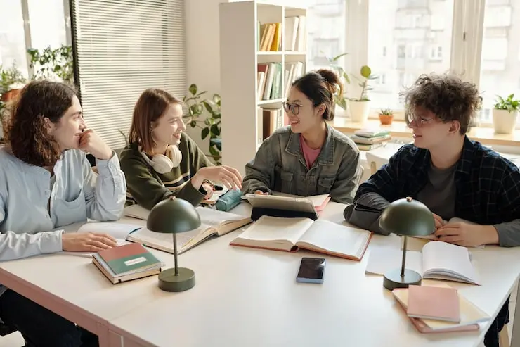 Four students collaborating on a study project at a desk with notebooks and a laptop